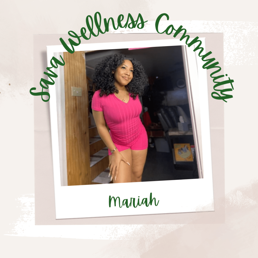 The words “Sava Wellness Community” are written in green cursive script over top of a polaroid picture. The polaroid picture is sitting on top of multiple layers of pink, cream, and white watercolour background. The polaroid picture has the name “Mariah” written in green under it. The picture is of Mariah smiling and staring off to the right of the camera. Mariah is wearing a pink jumpsuit, a gold bracelet on her right wrist, and has her hair down.