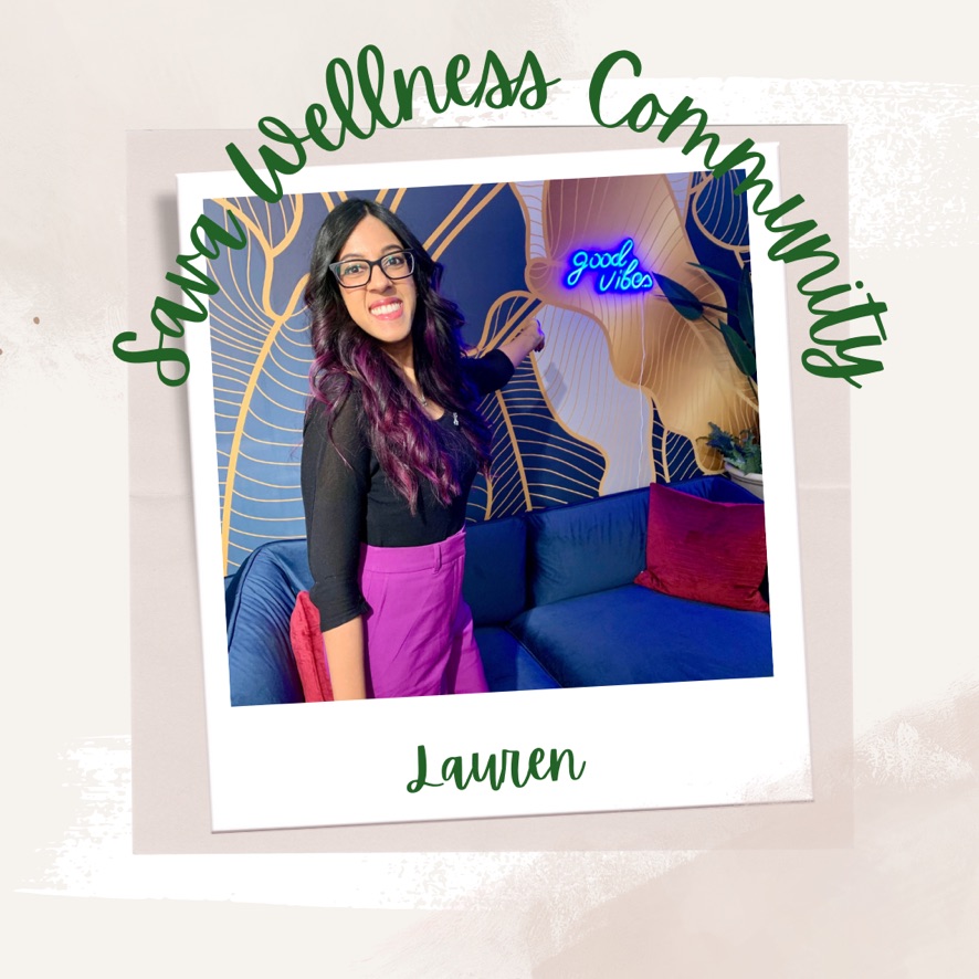The words “Sava Wellness Community” are written in green cursive script over top of a polaroid picture. The polaroid picture is sitting on top of multiple layers of pink, cream, and white watercolour background. The polaroid picture has the name “Lauren” written in green under it. Lauren is smiling at the camera and it pointing behind her to a light-up blue sign on the wall that says “good vibes”. Lauren is wearing glasses, has her long black and purple hair curled, and is wearing a black ¾ sleeve shirt and purple pants.]